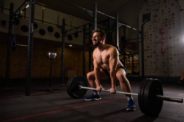 Gömleksiz beyaz adam spor salonunda kaldırma yapıyor.. 