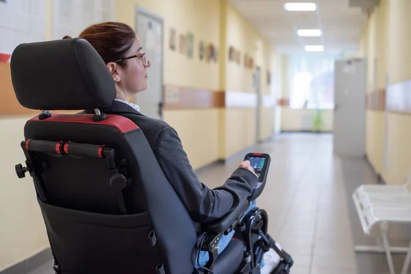 Caucasian woman in electric wheelchair in university corridor.