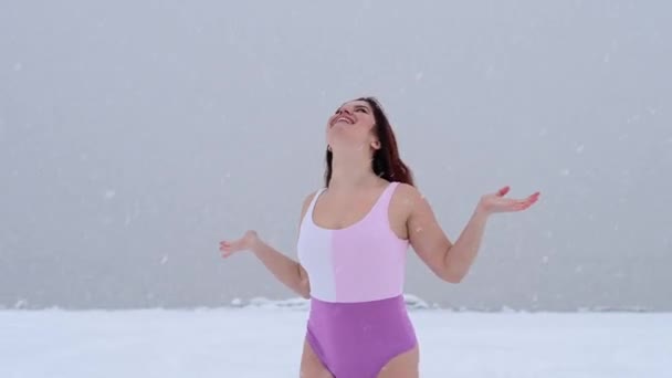 Šťastná žena v plavkách chytí padající sněhové vločky v blízkosti zamrzlého jezera. — Stock video