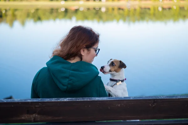 Caucasian woman sits on a bench with a dog by the lake. — Stock Photo, Image