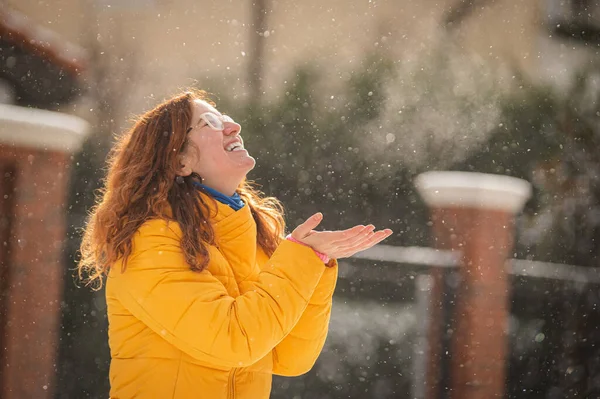 Ruiva mulher caucasiana se alegra no inverno e pega flocos de neve com as palmas das mãos. — Fotografia de Stock