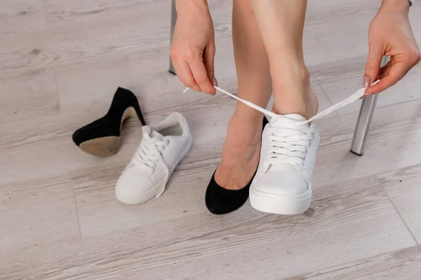 Close-up mujer de negocios se quita los zapatos se pone zapatillas de deporte de cuero blanco. —  Fotos de Stock
