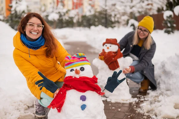 Två ansiktslösa vita kvinnor gör en snögubbe. Flickvänner ha kul på vintern. — Stockfoto