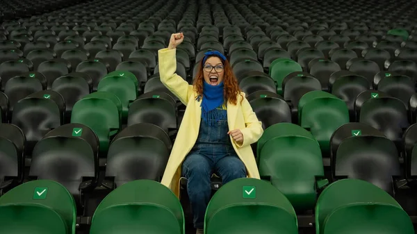 Vit kvinna hejar på ett idrottslag på stadion. Flickan tittar på matchen på arenan ensam. — Stockfoto