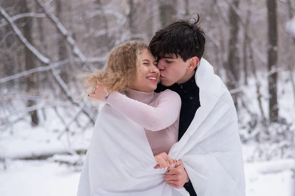 Un jeune couple se promène dans le parc en hiver. Le mec et la fille s'embrassent enveloppés dans une couverture blanche à l'extérieur. — Photo