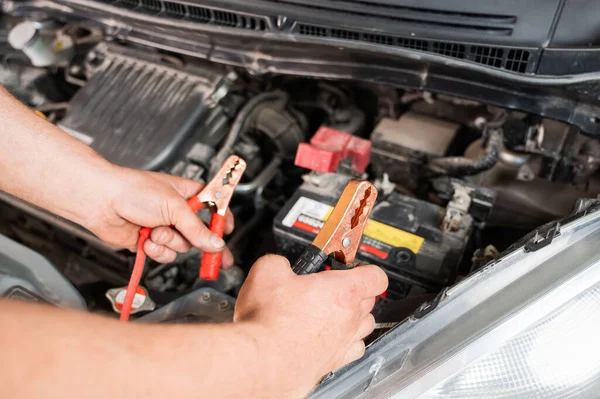 O mecânico conecta os grampos à bateria do carro descarregado. — Fotografia de Stock