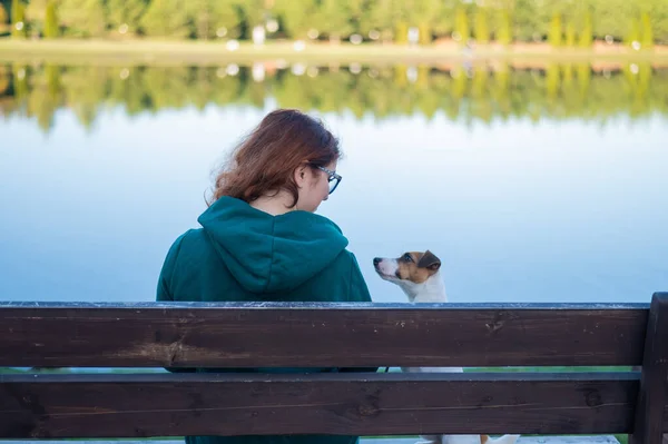 白人女性は湖のそばの犬とベンチに座っている. — ストック写真