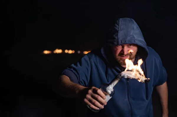 Kapüşonlu adam yanan bir şişe tutuyor. Molotof kokteyli. — Stok fotoğraf