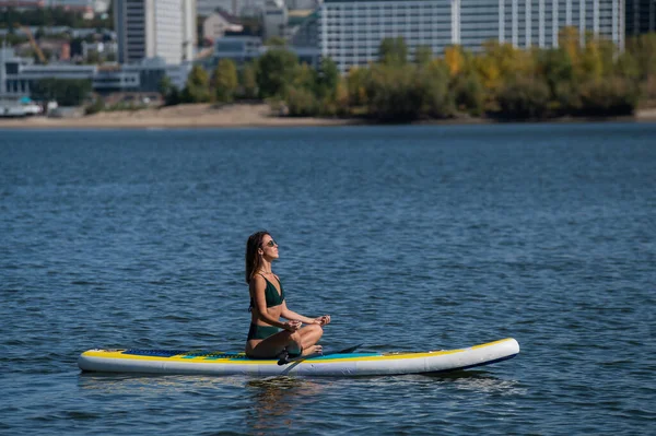 Mujer caucásica está montando una tabla de SUP en el río en la ciudad. Deportes de verano. —  Fotos de Stock