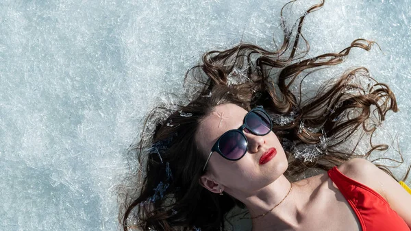 Close-up portrait of a caucasian woman lying on the snow in sunglasses. Top view. — Stock Photo, Image