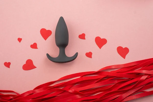 Close-up of a black butt plug and hearts and a red lash on a pink background. Symbol of love and passion. — Stock fotografie