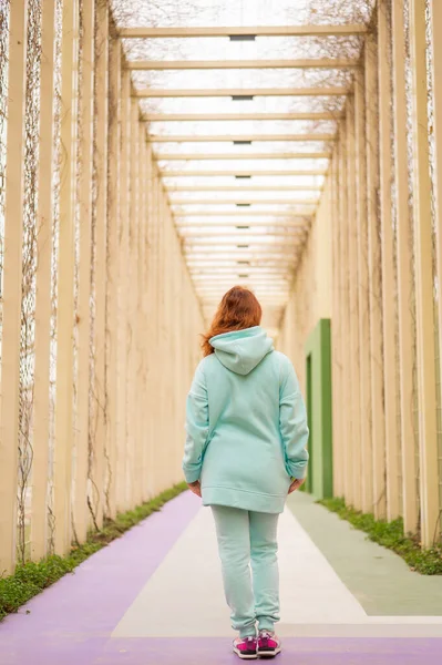 Kaukasische roodharige vrouw in een munt hoodie wandelen in het park. — Stockfoto