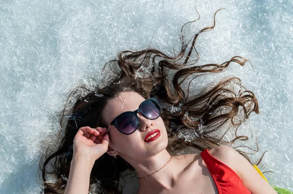 Gros plan portrait d'une femme caucasienne allongée sur la neige en lunettes de soleil. Vue du dessus. — Photo