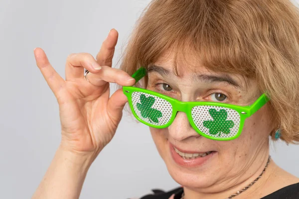 Porträtt av en leende äldre kvinna klädd i klöver-mönstrade glasögon för st patricks dag — Stockfoto