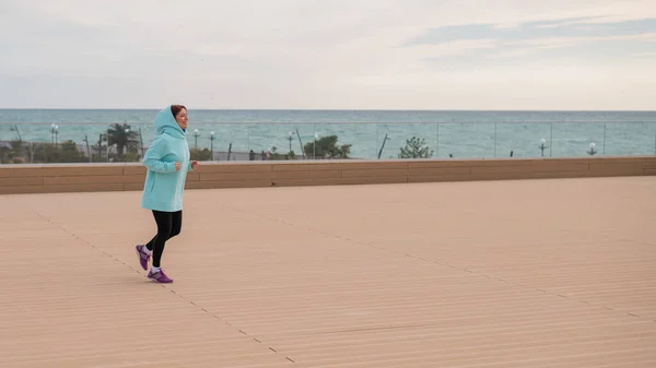 Femme blanche dans un sweat à capuche jogging sur le bord de la mer. — Photo