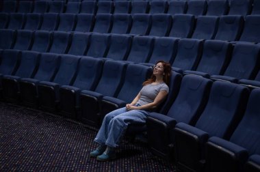 Kafkasyalı kızıl saçlı kadın boş bir salonda sinemada ön sırada oturuyor. Kız tek başına film izliyor.. 