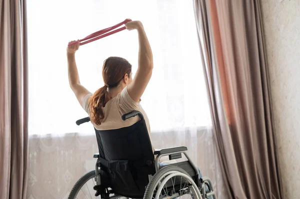 Mujer caucásica en silla de ruedas haciendo ejercicios con la ayuda de bandas de goma de fitness. — Foto de Stock