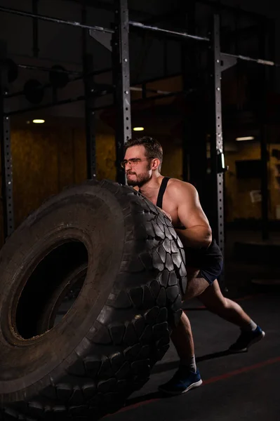 Caucasian man pushing a car tire in the gym. — Stock Photo, Image