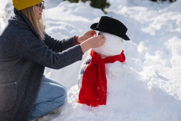 Vit kvinna skulpterar en snögubbe ur snön. Moroten är platsen för näsan.. — Stockfoto