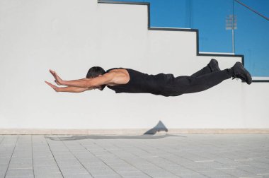 Siyah spor kıyafetli bir adam dışarıda şınav çekerken zıplıyor..