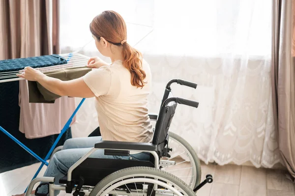 Blanke vrouw in een rolstoel hangt natte was op een droger. — Stockfoto