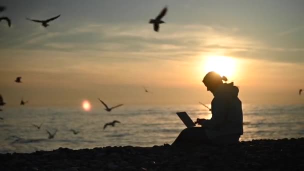 Mujer caucásica escribiendo en un portátil en la orilla del mar al atardecer. Trabajo independiente. — Vídeos de Stock