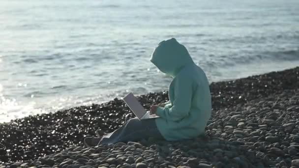 Mujer caucásica escribiendo en un portátil en una costa rocosa. Trabajo independiente. — Vídeos de Stock