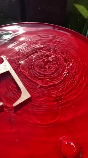 Close-up pioggia gocciola su uno sfondo rosso e lascia cerchi sull'acqua. — Video Stock