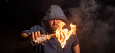 Kapüşonlu adam yanan bir şişe tutuyor. Molotof kokteyli