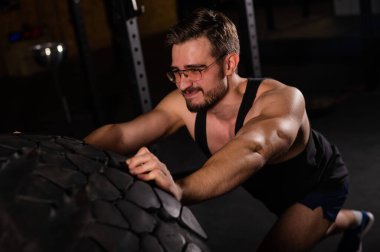 Beyaz bir adam spor salonunda araba lastiği itiyor.. 