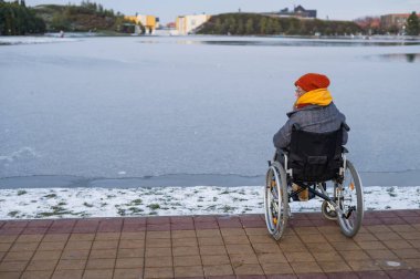 Tekerlekli sandalyedeki beyaz kadın kışın gölün kenarında yürür..