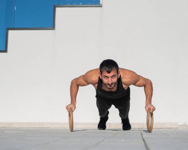 Siyah spor kıyafetli bir adam dışarıda ring şınavı çekiyor..