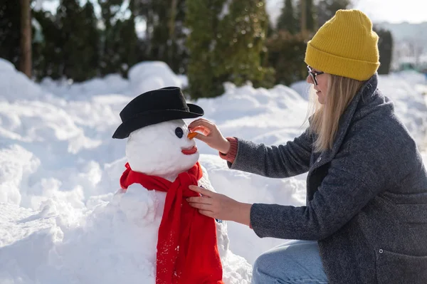 Vit kvinna skulpterar en snögubbe ur snön. Moroten är platsen för näsan.. — Stockfoto