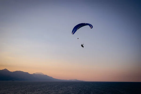 Silhueta de um homem em um parapente voando sobre o mar ao pôr do sol. — Fotografia de Stock