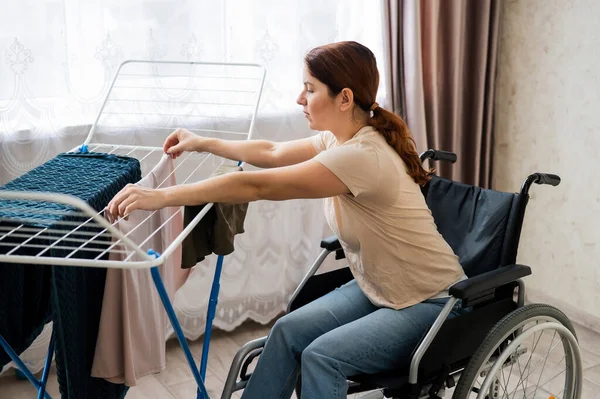 Blanke vrouw in een rolstoel hangt natte was op een droger. — Stockfoto