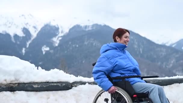 Biała kobieta na wózku inwalidzkim w śnieżnych górach. Szczęśliwa dziewczyna podnosi ręce na boki i myśli, że lata. — Wideo stockowe