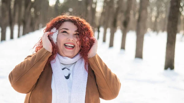Пухнаста жінка слухає музику в навушниках під час прогулянки в парку взимку . — стокове фото