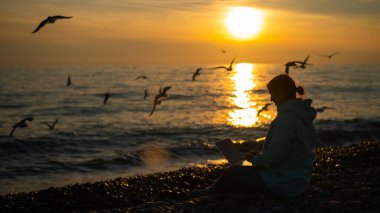 Gün batımında deniz kıyısında dizüstü bilgisayarda yazan beyaz bir kadın. Serbest çalışma..