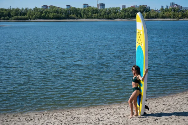 Blanke vrouw loopt langs het strand en draagt een bord aan de rivier in de stad. Zomer sport. — Stockfoto