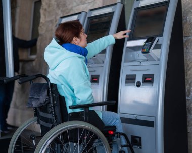 Tekerlekli sandalyedeki beyaz bir kadın tren istasyonundaki self servis kasasına ulaşamaz. Ulaşılması zor bir ortam.
