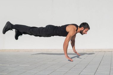 Siyah spor kıyafetli bir adam dışarıda şınav çekerken zıplıyor..