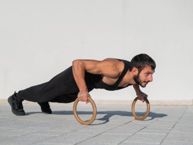 Siyah spor kıyafetli bir adam dışarıda ring şınavı çekiyor..