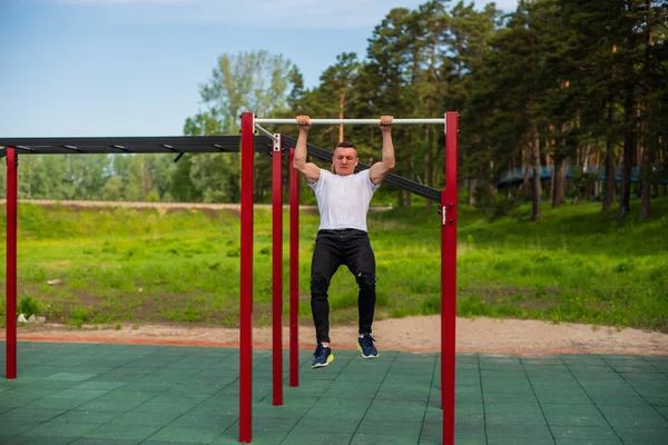 Caucásico hombre tira de sí mismo en una barra horizontal en un campo de deportes. — Foto de Stock