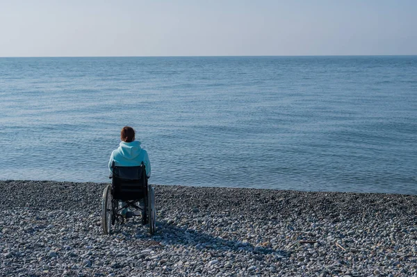 Femme blanche en fauteuil roulant sur une plage de galets au bord de la mer. — Photo
