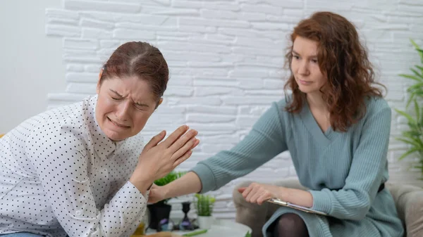 Blanke vrouw huilt bij psychotherapie. De vrouwelijke arts kalmeert de patiënt en houdt haar hand vast. — Stockfoto