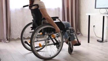 Tekerlekli sandalyedeki beyaz bir kadın masasına doğru geliyor ve evden bir dizüstü bilgisayarla yazmaya başlıyor. Engelliler için uzak çalışma.