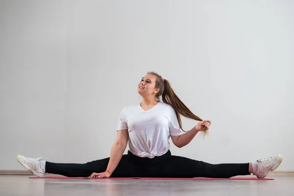 Knubbig ung kvinna gör stretching på vit bakgrund. — Stockfoto