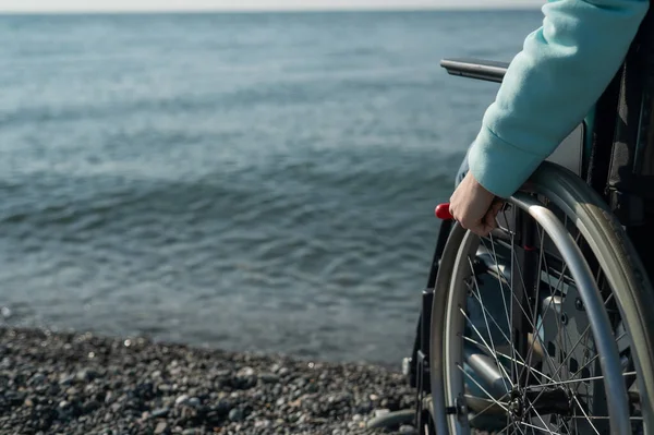 Vit kvinna i rullstol på stranden. Närbild av kvinnliga händer. — Stockfoto