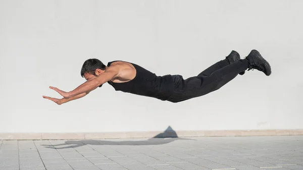 En mand i sort sportstøj hopper, mens du gør push-ups udendørs. - Stock-foto