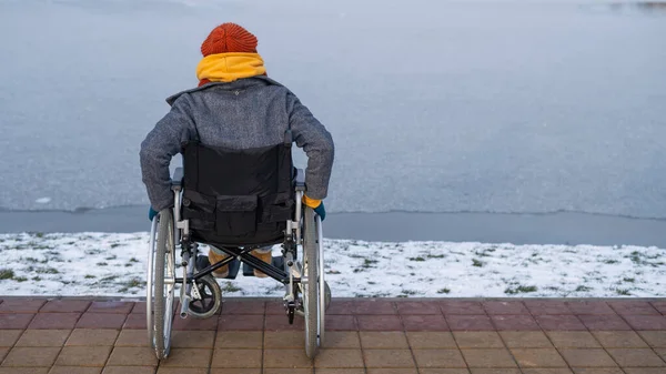 Vit kvinna i rullstol går vid sjön på vintern. — Stockfoto